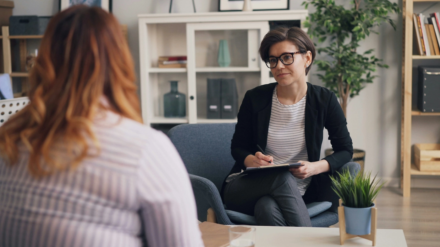 Photo of 2 women sitting on separate sofas opposite each other listening to each other. Our featured image for our article on 'cognitive behavioural therapy for gambling'