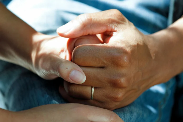 Close up photo of 2 people holding hands in a supportive way. Our featured image for our article on 'holistic gambling recovery'